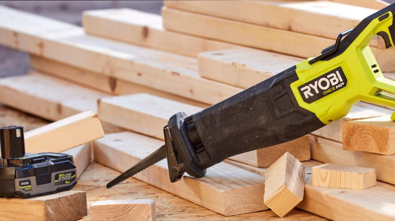 A Ryobi reciprocating saw resting on cut wood next to a Ryobi battery.
