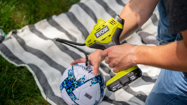 A man pumping up a soccer ball with a Ryobi inflator