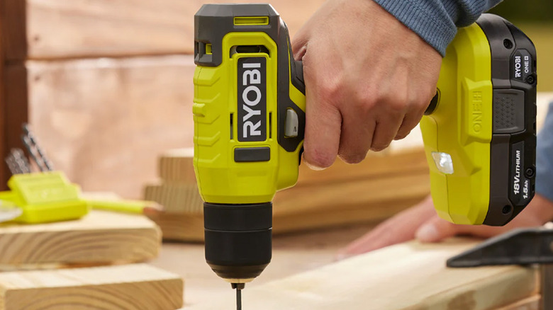 A man drilling a hole into a piece of wood with a Ryobi drill