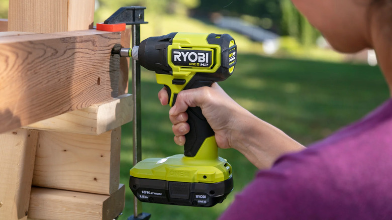 A woman drilling into a piece of wood outside on a sunny day