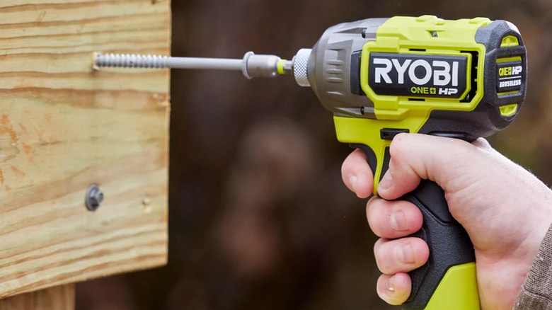 A person using a Ryobi impact driver to drill a long screw into wood.