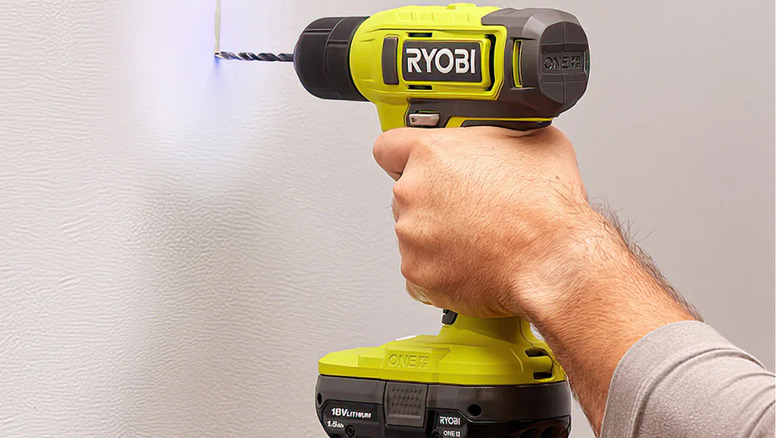 A man drilling a hole into drywall with a Ryobi drill