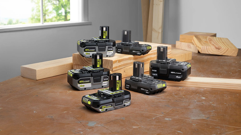 Six Ryobi batteries in varying sizes on a workshop table.