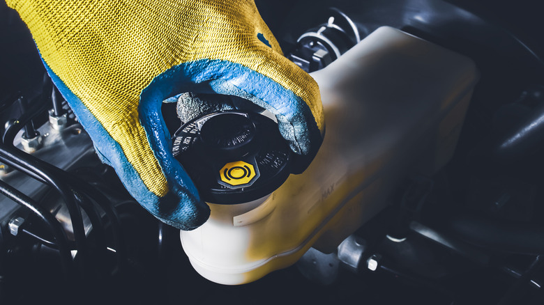 Gloved hand opening a car's brake fluid reservoir.