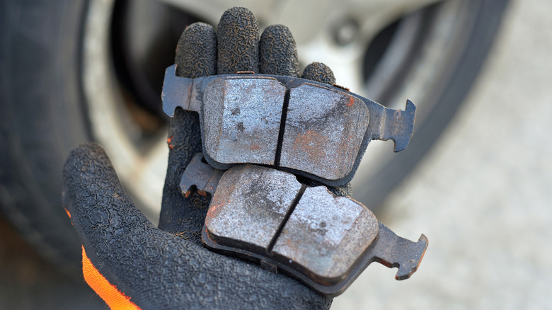 Gloved hand holding worn out brake pads.