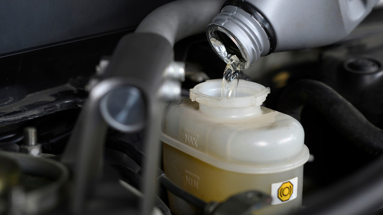 Pouring brake fluid into a car's brake fluid reservoir.