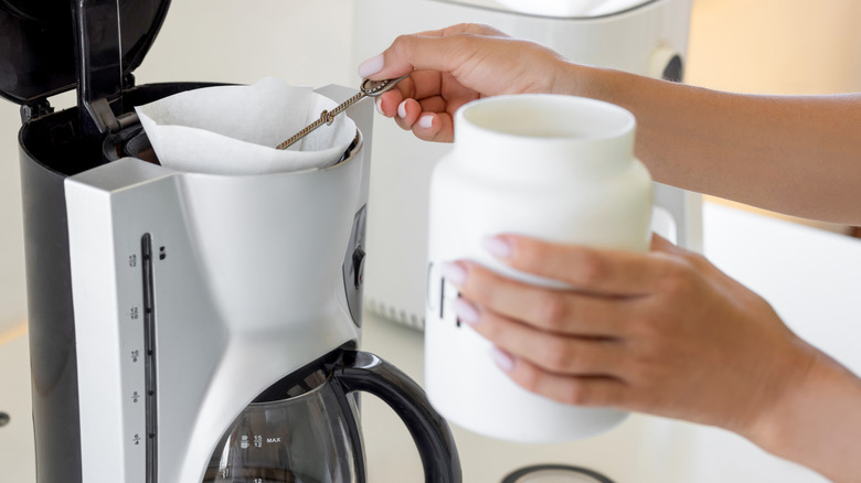 A woman putting coffee grounds in a drip coffee machine