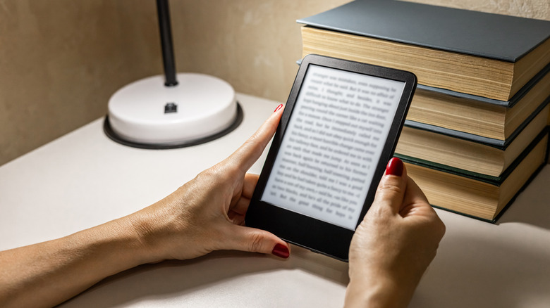 A person reading an e-reader under a lamp