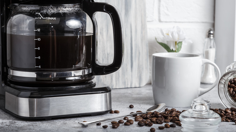 A drip coffee maker on a counter top with a cup and some coffee beans