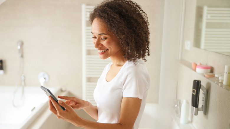 A woman smiling looking at her phone in a bathroom