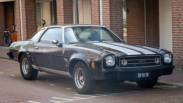 A 1973 Chevrolet Chevelle Laguna finished in black, complete with dual-white racing stripes, parked at the side of a road.