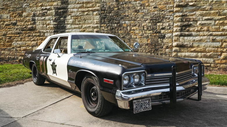 A 1974 Dodge Monaco standing outside a beige brick building, complete in police decals.