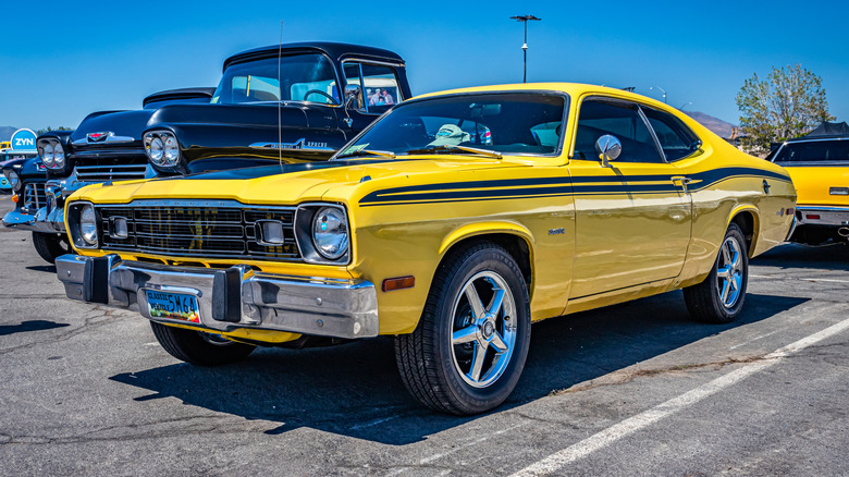 A 1973 Plymouth Duster of the coupe body style parked on concrete outdoors at a car show in the afternoon.