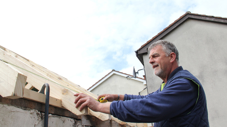 Man measuring roof beams with tape measure