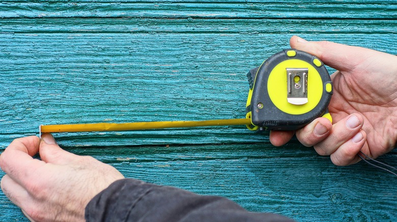 Hands extending tape measure on blue wooden background