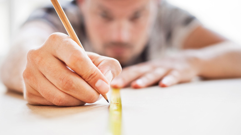 Man making marks with pencil alongside tape measure
