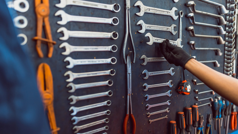 Gloved hand reaching onto a wall on which a wrench set is attached.