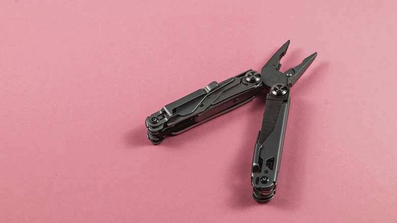 A portable multi tool on a pink surface.
