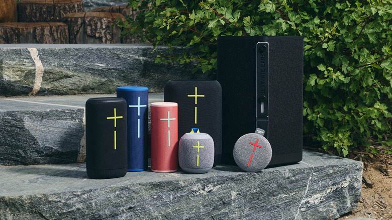 Seven assorted Ultimate Ears speakers on rock steps with foliage behind