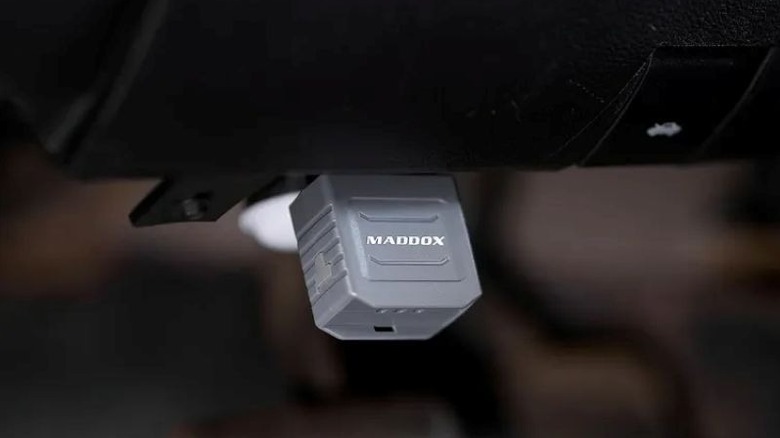 A small dongle attached to the OBDII connection under a vehicle's dashboard