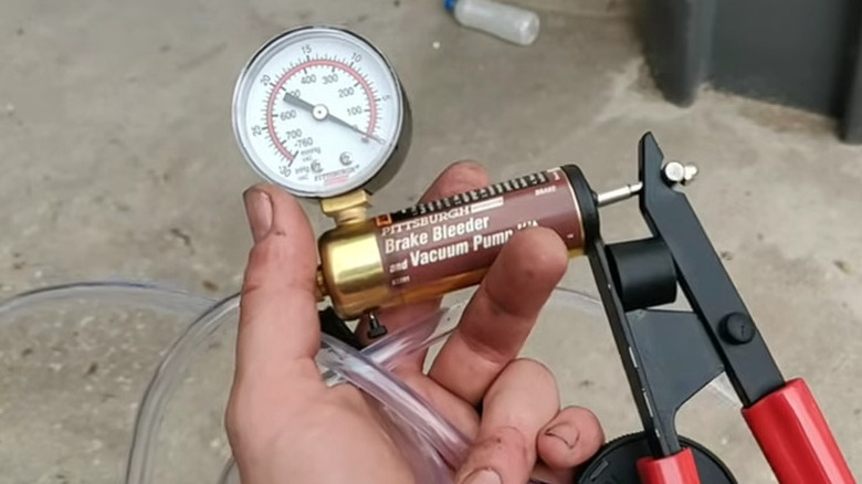 Hand holding a manual brake bleeding tool with a large dial and clear hose
