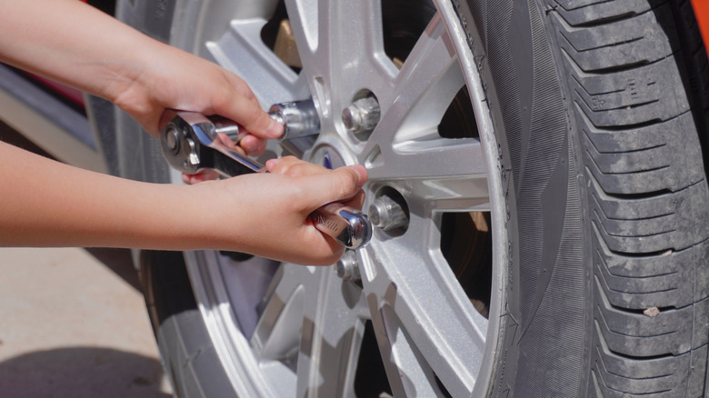 A person loosening lug nuts on a tire