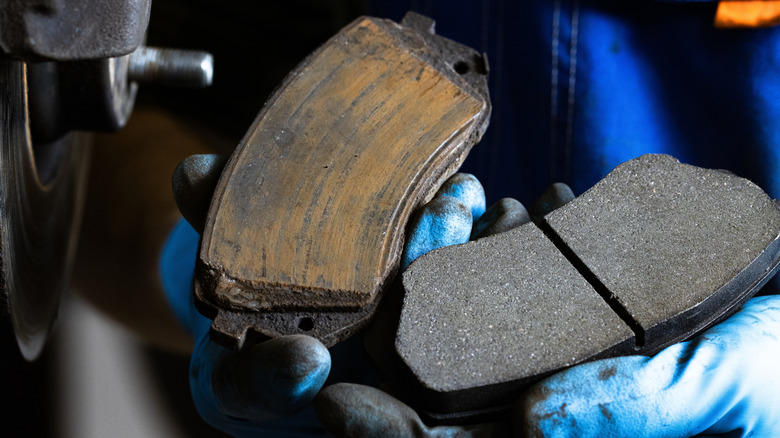 A person holding a worn brake pad in one hand and a new one in the other