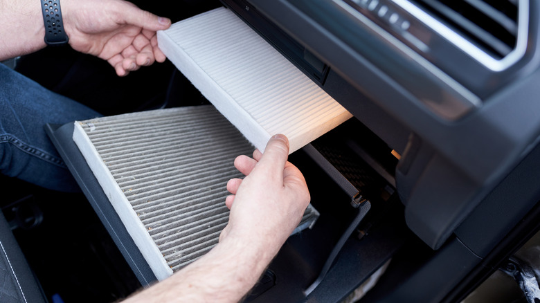 A person swapping out an old cabin filter in their vehicle cabin.