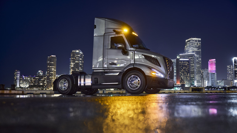 Silver Volvo VNR 300 semi-truck cab seen from left against night cityscape