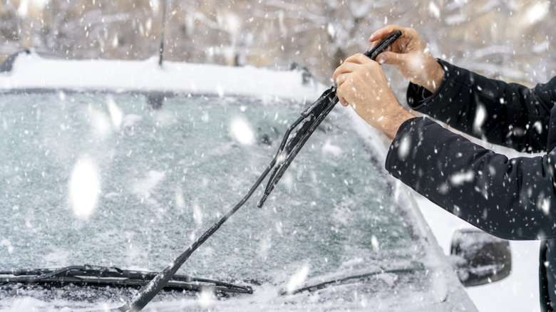 Person cleaning windshield wiper blade in the snow.