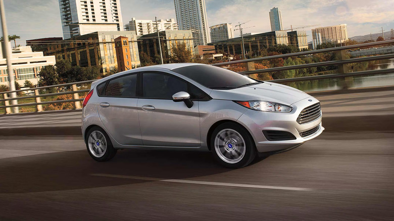 Silver Ford Fiesta on a roadway with buildings behind it