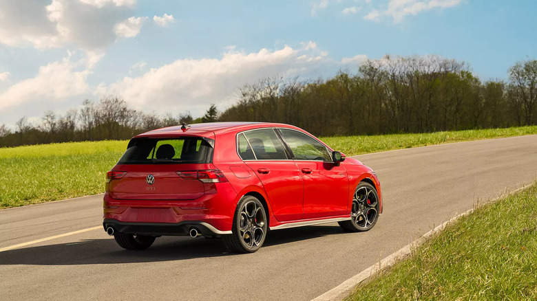 Rear and side view of red Volkswagen Golf GTI on a roadway with grass on both sides