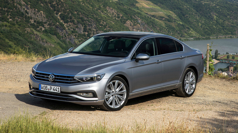 Silver VW Passat parked on dirt with green hills and water behind