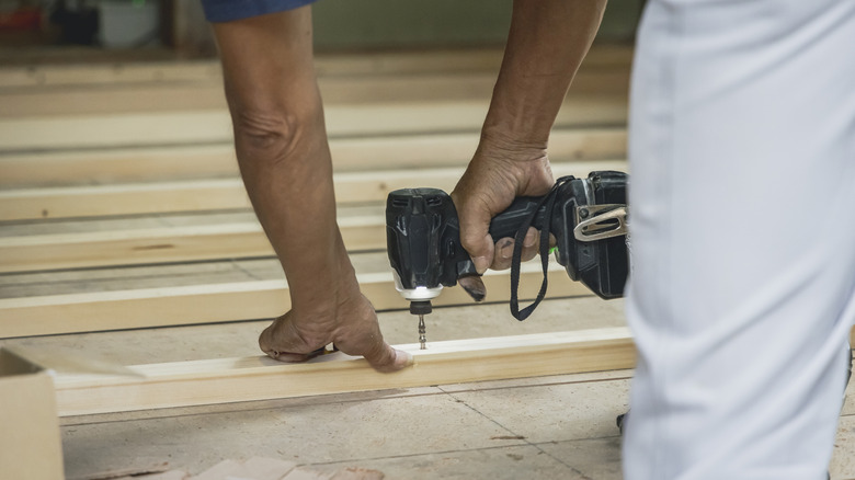 A worker using an impact driver on wood.