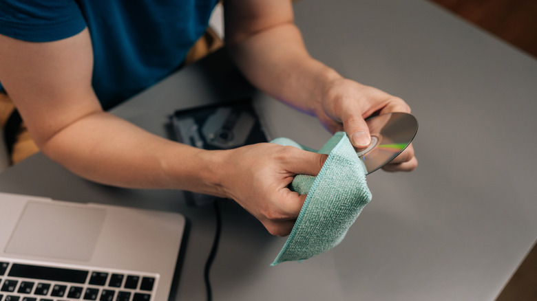Person sitting at a table wiping a CD with a microfiber cloth