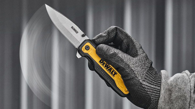 A DeWalt folding knife being flipped out by a hand with a gray glove