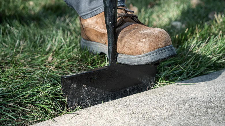 A man pushing an edger into the grass near a sidewalk