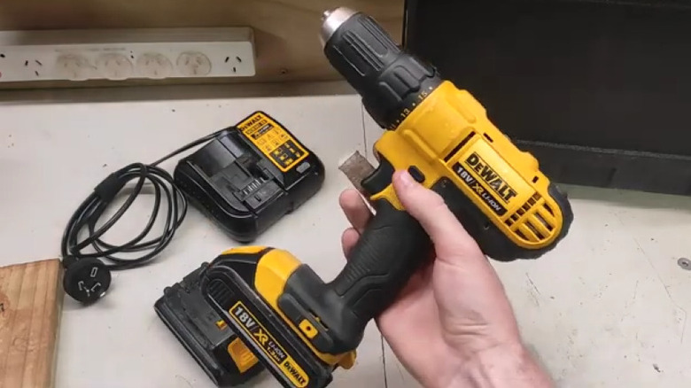Person holding drill over charger and battery