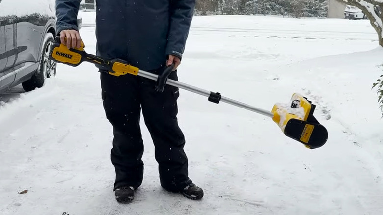 Person holding electric snow shovel on a snowy driveway