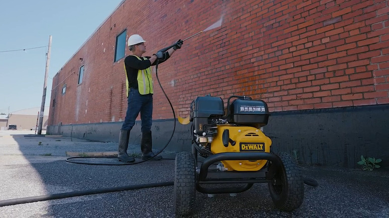 Person using pressure washer on brick wall