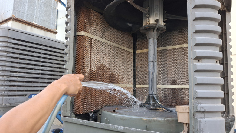 Person's hand spraying water from a hose into an opened up swamp cooler