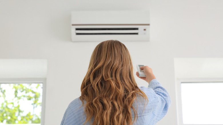 Person facing away from the camera pointing a remote at a wall-mounted mini split AC unit