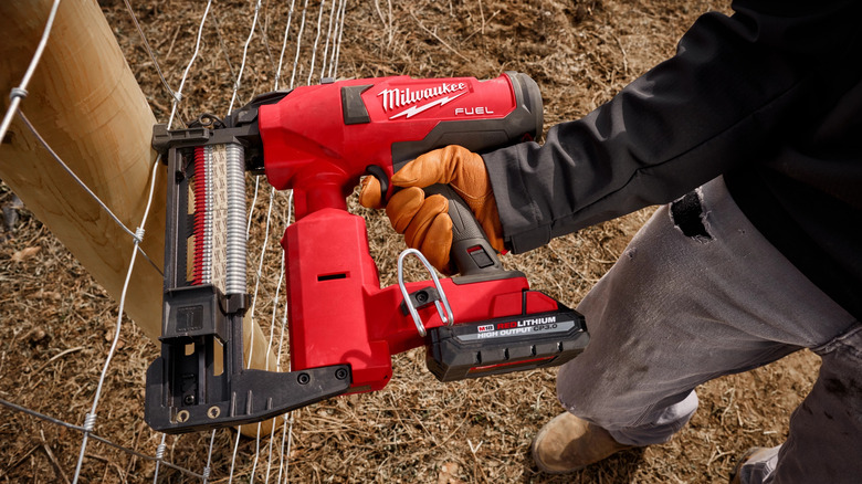 A worker using the Milwaukee M18 FUEL Utility Fencing Stapler to secure metal fencing to a post