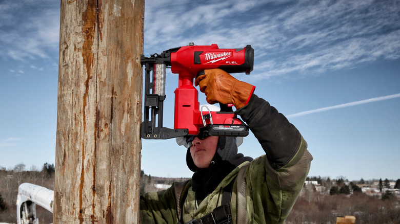 A lineman in safety gear using the Milwaukee M18 Fuel Utility Fencing Stapler on a telephone pole