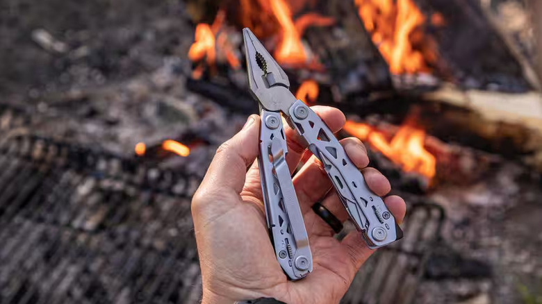 Gerber Suspension NXT multi-tool held in hand near camp fire.