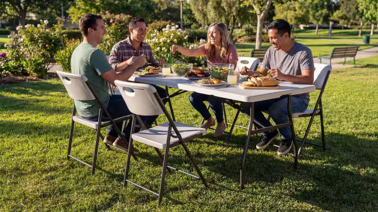 Family sits around an HDX6 Foot Almond Resin camping table in a garden.