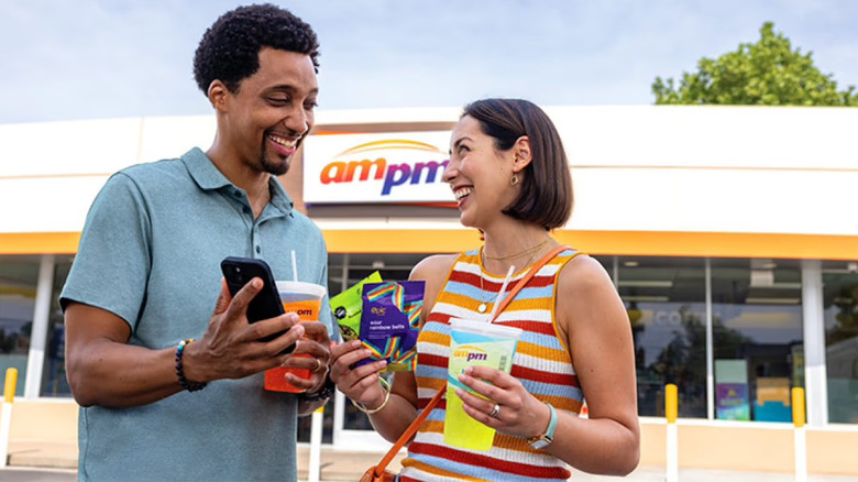 Two people in front of an ampm store