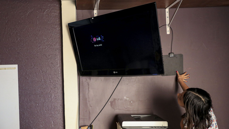 An LG TV with an indoor antenna placed on the wall behind it