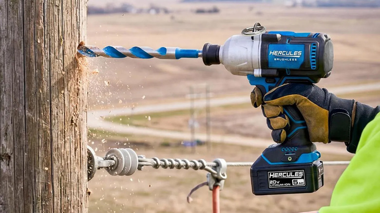 A worker drilling a hole into a fence post.