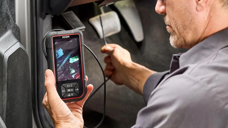 A mechanic using an inspection camera to check the footwell of a car.